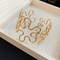 Detail of a wavy gold hollow flower cuff bracelet resting inside a beige jewelry box - Arm Cuff / Gold