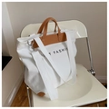 Weiße Canvas-Tasche mit braunen Lederdetails und breitem Gurt auf einem Metallstuhl - Weiß