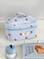 Détails du motif fraise matelassé et de l'écusson sur une trousse de toilette à rayures bleues - Sac cosmétique à main