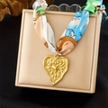 Dettaglio del ciondolo a cuore dorato con nastro in seta colorata su portagioie - Ciondolo Cuore Blu Verde (N3607)