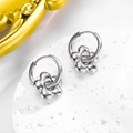Detail of silver metallic hoop earrings with 3D five-petal flower charms on white display - Earrings / Silver