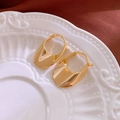Primer plano de pendientes de aro ovalados dorados con acabado de espejo en un plato - Pendientes Huggie de Bolso Ovalados Dorados