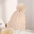 Close-up of beige knit beanie with cable pattern and large faux fur pom-pom detail - Beige