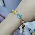 Detail of a gold heart bracelet with colorful enamel and sparkling zircons on a wrist - Colorful