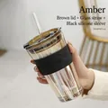 Amber straw glass breakfast cup with black silicone sleeve and lid in hand-held view - Amber + Tea Lid + Clear Glass Straw + Black Silicone Sleeve