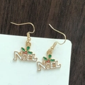 Detail of Christmas Noel earrings with gold trim and white enamel on a wood surface - Christmas Letter NOEL