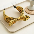 Dettaglio del cerchietto giallo con stampa paisley e nodo su vassoio con decoro rustico - Giallo brillante