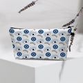 Close-up of white Evil Eye makeup bag on white stand with lavender decorative accents - White Long Lashes Eye