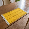 Bohemian yellow knit table runner with white tassels on a rustic dark wood dining table - Woven Yellow