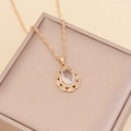 Golden teardrop necklace with crystal pendant on a beige jewelry box lid - Clear White