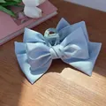 Dettaglio di un fermaglio per capelli a doppio fiocco in raso azzurro su tavolo in legno - Fermaglio a fiocco bifacciale / Blu