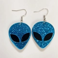 Close-up of blue glitter resin alien earrings with silver hooks for Halloween style - Sequin Blue