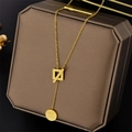 Gold titanium necklace with square and Good Luck round pendants on jewelry box - Gold