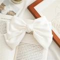 Elegant oversized white satin bow hair clip placed on a vintage book for styling - White
