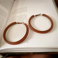 Detail of reddish-brown leather wrapped hoop earrings on a book page with vintage texture - Coffee Leather (Silver Pin)