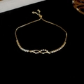 Dettaglio del bracciale tennis dorato regolabile con charm infinito in zirconi e cursore - Stile Onda Incrociata / Croce Oro