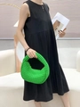 Detail of bright green woven crescent handbag held by a woman in a black dress - Green