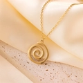 Detalle de un collar con colgante de espiral dorado sobre seda crema y piedra - Dorado