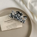 Detail shot of a large marble pattern hair claw clip on a decorative plate and silk fabric - Black and White Leopard Print
