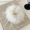 Close-up of a white fluffy feather hair scrunchie placed on a beige linen book cover - Beige