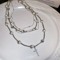 Detalle del collar multicapa plateado con colgante de cruz y perlas en bandeja cerámica - Collar Multicapa de Cruz de Plata