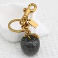 Black glitter apple keychain with golden leaf charm and lobster clasp on white fabric - Gun Black Apple with Bronze Gold