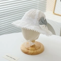 Detailed view of white lace baby sun hat with a grey polka dot bow on a stand. - 50-52CM / White