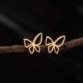 Pendientes de mariposa dorados minimalistas presentados sobre una rama de madera natural - Dorado
