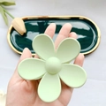 Close-up of matte mint green flower hair claw clip held over a ceramic decorative plate - Green