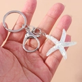 Macro shot of iridescent starfish keychain with silver metal ring held in hand - White Starfish