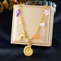 Goldene Halskette mit Muschel- und Herzanhängern auf einer beigefarbenen Schmuckbox - Lila Kreuz Conch Delfin Halskette (N3535)