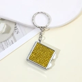 Close-up of square metal keychain with yellow rhinestones on a beige surface - Yellow