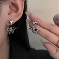 Nahaufnahme der silbernen Herz-Ohrstecker mit schwarzen Schmetterlings-Anhängern aus Metall - Silberner Schmetterling