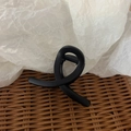 Close-up of black matte twisted hair claw clip on a rustic woven rattan background - Frosted Black
