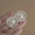 Close-up of a silver petal earring with a central pearl held against a warm beige background - 14# Silver Radial Texture Pearl Studs (HE15735)