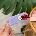 Sweet purple teddy fleece hair clip with cute buttons and bow held against a green leaf - Purple