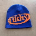 Close-up of blue knitted beanie with orange filthy typography on grey concrete - One Size / Royal Blue