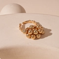 Macro shot of gold sphere cluster ring on white textured stand in warm lighting - Open Ring / Gold