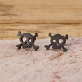 Close-up of black punk skull stud earrings crafted from stainless steel on a stone base - Crossbones Skull / Black