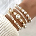 Detalle de un juego de cuatro pulseras de perlas con dije de corazón dorado en la muñeca - Corazón Dorado - Juego de Perlas Blancas