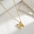 Macro detail of puffy golden initial M pendant necklace with a polished 3D metal finish - Letter M