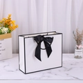 White cardboard gift bag with large black bow and ribbon handle on marble surface - 28*20*10cm / White with Black Edge + Black Ribbon