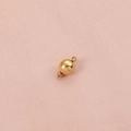 Primer plano de un cierre magnético dorado de 8mm sobre fondo de tela rosa con textura - Imán redondo / Dorado