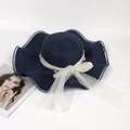 Detail of navy blue straw sun hat with wavy brim, pearl mesh bow, and elegant texture - Dark Blue