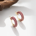 Detail von goldenen Creolen mit Pavé-besetzten rosa Zirkonia auf einem Holzständer - Rosa-Lila