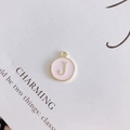 Macro shot of pink enamel round pendant with golden letter J for DIY jewelry making - Letter J