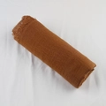 Brown cotton linen scarf with frayed edges rolled on a white textured fabric - Camel