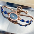 Macro detail of rose gold oval watch featuring blue dial and leaf-shaped gemstones - Blue