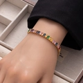 Rainbow baguette-cut zircon tennis bracelet in gold finish worn on wrist over beige texture - Multicolor Medium Rectangle