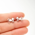 Close-up of silver galloping horse stud earrings with heart cutout held between fingers - Steel